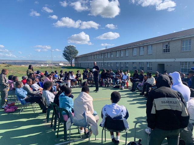 An outdoor session with learners seated on a school sports court